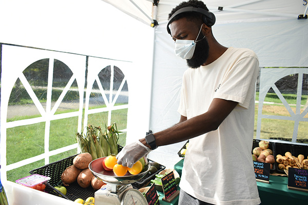 Man weighs vegetables a a farmers market in a tent