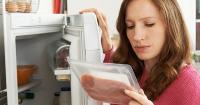 woman looks at meat in her fridge