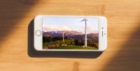 Image: cell phone on table with photo of wind turbines in mountainous region. Title: Verizon Flunks Green America's Scorecard Grading Wireless Companies on Clean Energy