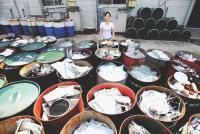 Image: woman standing with full recycling containers. Topic: Americans are bad at recycling. Here's How the World Does It Better.