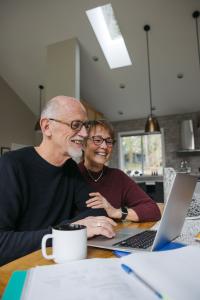 elderly couple looking at a computer screen, smiling. 