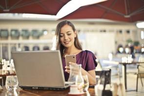 Image: woman on both smartphone and laptop. Title: Green America and T-Mobile Push AT&T and Verizon to Match T-Mobile’s 100% Renewable Energy Commitment