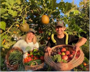 John and Holly in their Climate Victory Garden with baskets of vegetables 