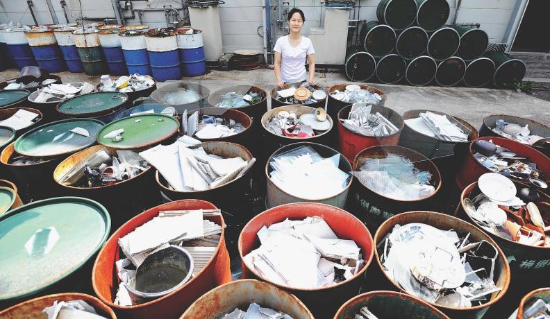 Image: woman standing with full recycling containers. Topic: Americans are bad at recycling. Here's How the World Does It Better.