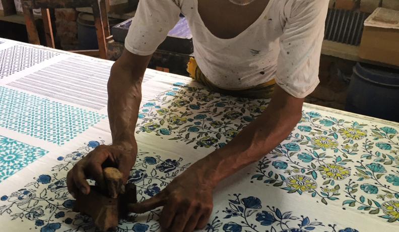 Indian man bends over a piece of cloth and applies a floral wood block print. Title: More than the Minimum: Why We Need a Livable Wage