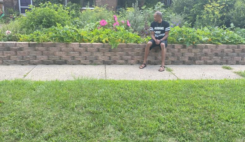 Yasir Allah, Aja Yasir's husband, sits in front of their house and climate victory garden in Gary, Indiana. Photo by Aja Yasir.