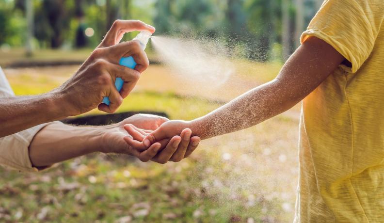 person spraying kid with natural bug spray outdoors