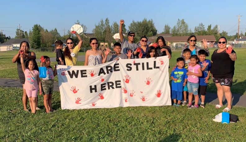 Indigenous activists holding a sign that reads "we are still here"