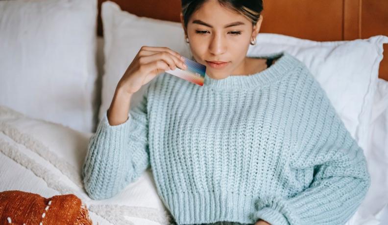 woman in a blue sweater holding her credit card while she shops online