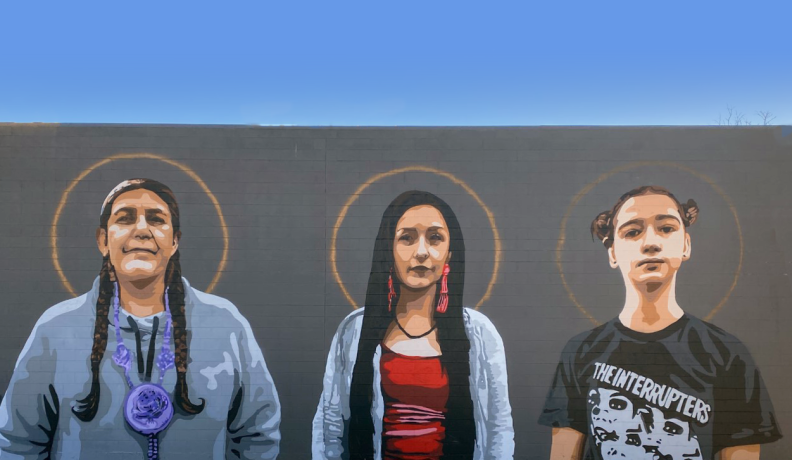 Mural painted on the outside of Native American Bank. There are three women of different ages standing side by side with halos around their heads to represent what Native American Bank honors and celebrates.