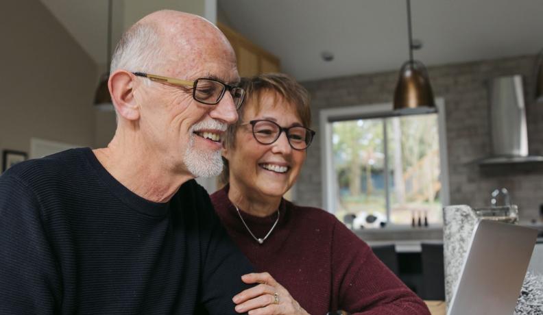 elderly couple looking at a computer screen, smiling. 