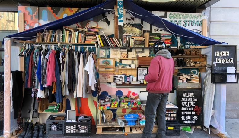 a person in a red jacket and black pants browsing the shelves of a Free Store in Green Point.