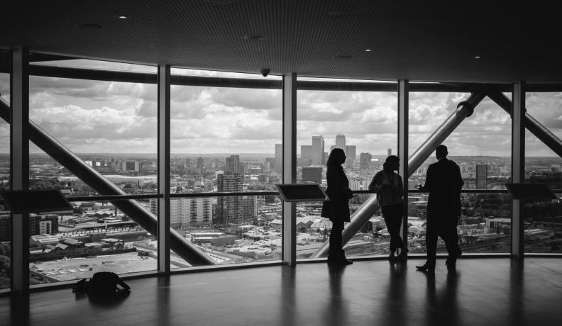 black and white photo of three people talking in front of a large panoramic window overlooking the city.