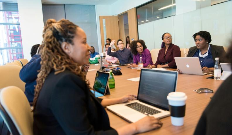 many women sitting around a conference table in an office setting. They appear to be discussing. 