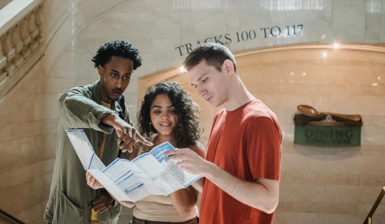 three young people looking at a train station times table.