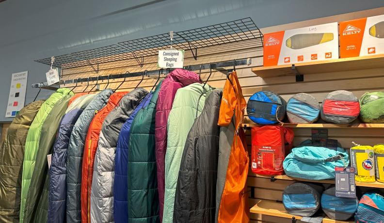 rows of gently used sleeping bags rest on hangers next to sleeping pads and camp pillows.