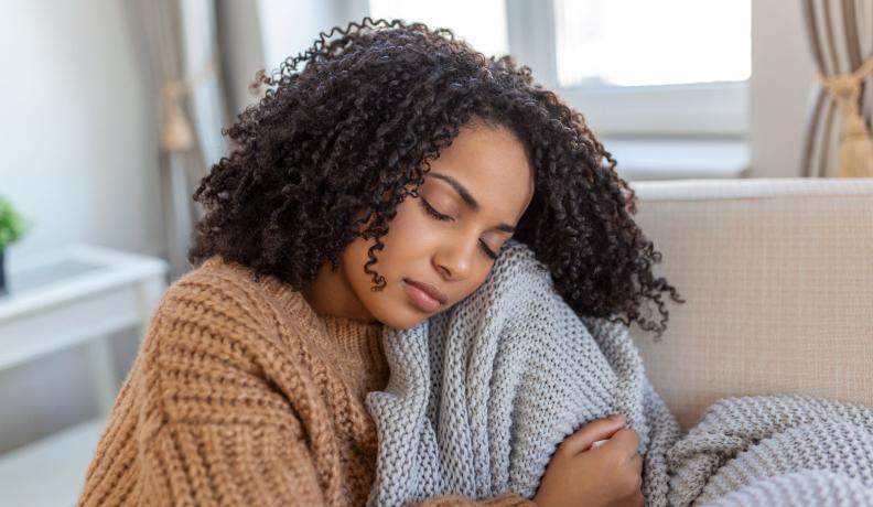 A Black woman relaxing and cuddling with a gray knitted blanket.