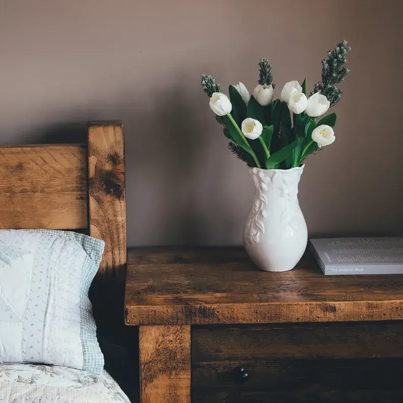 Image: side table with flowers, in bedroom. Topic: The Allergen-Free Bedroom