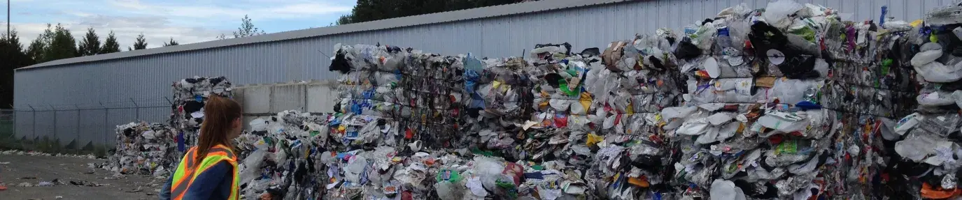 Image: person standing in front of large piles of recyclables. Topic: Does Recycling Help the Climate?