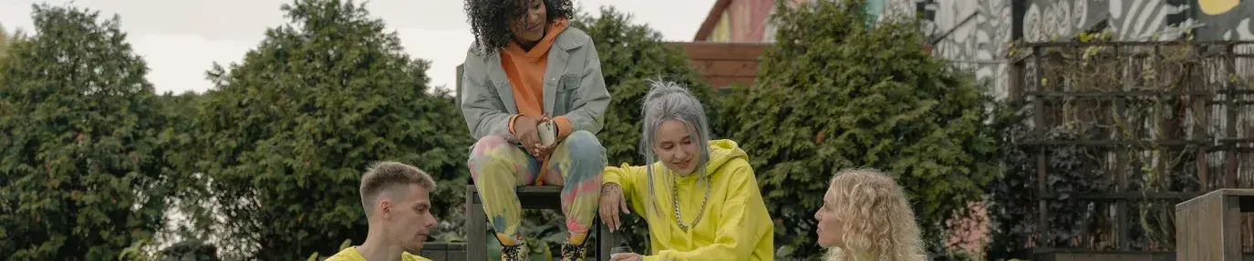 A brightly dressed group of young people sitting on large, concrete steps outside. They are talking. Gen Z finances.