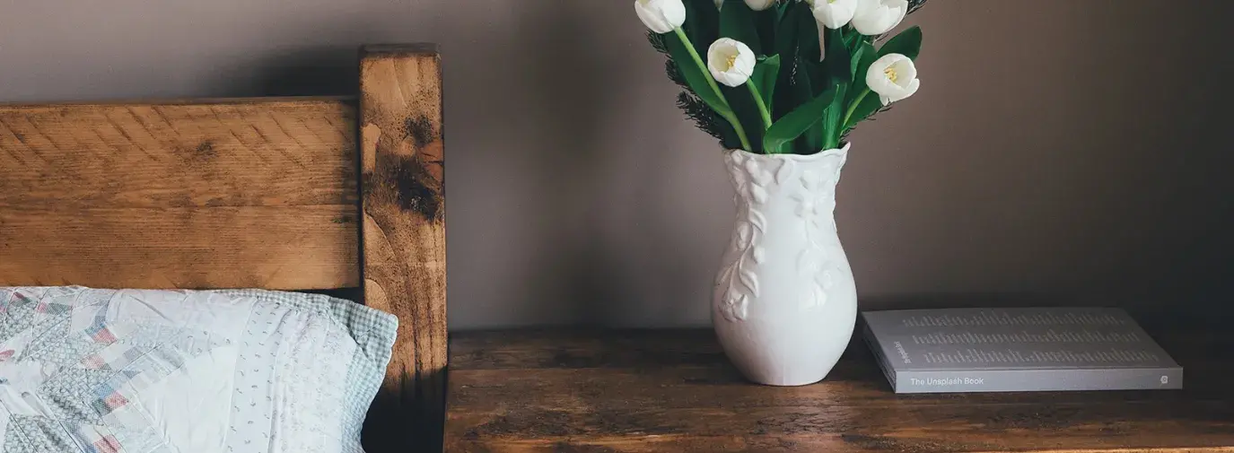 Image: side table with flowers, in bedroom. Topic: The Allergen-Free Bedroom