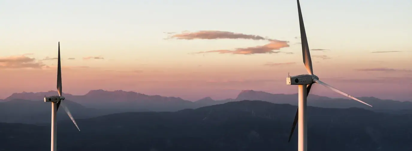 Image: wind turbines on a mountain ridge. Article: How to Advance Green Energy