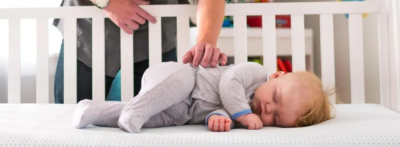 Image: father smiling over baby in crib. Organic baby products.