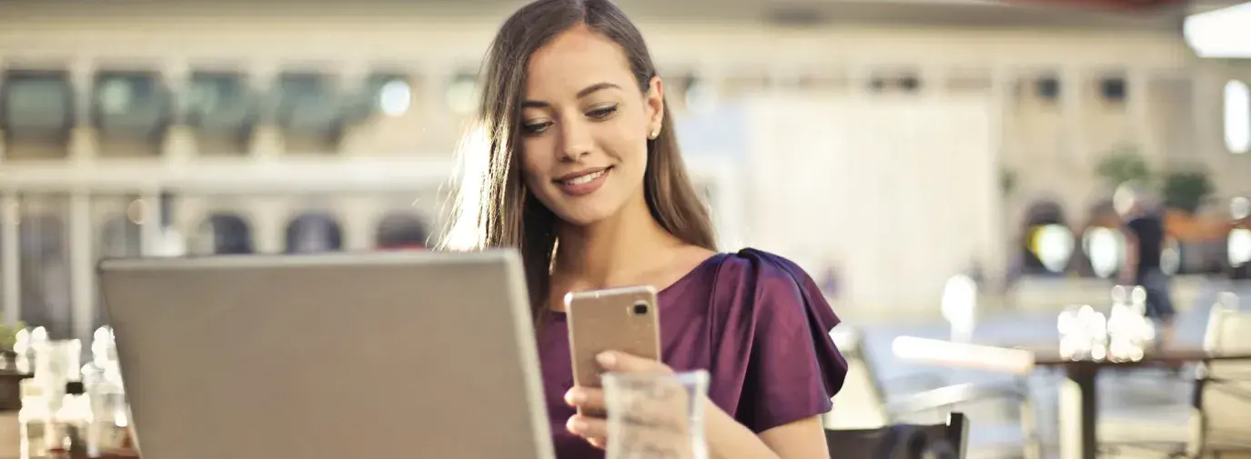 Image: woman on both smartphone and laptop. Title: Green America and T-Mobile Push AT&T and Verizon to Match T-Mobile’s 100% Renewable Energy Commitment