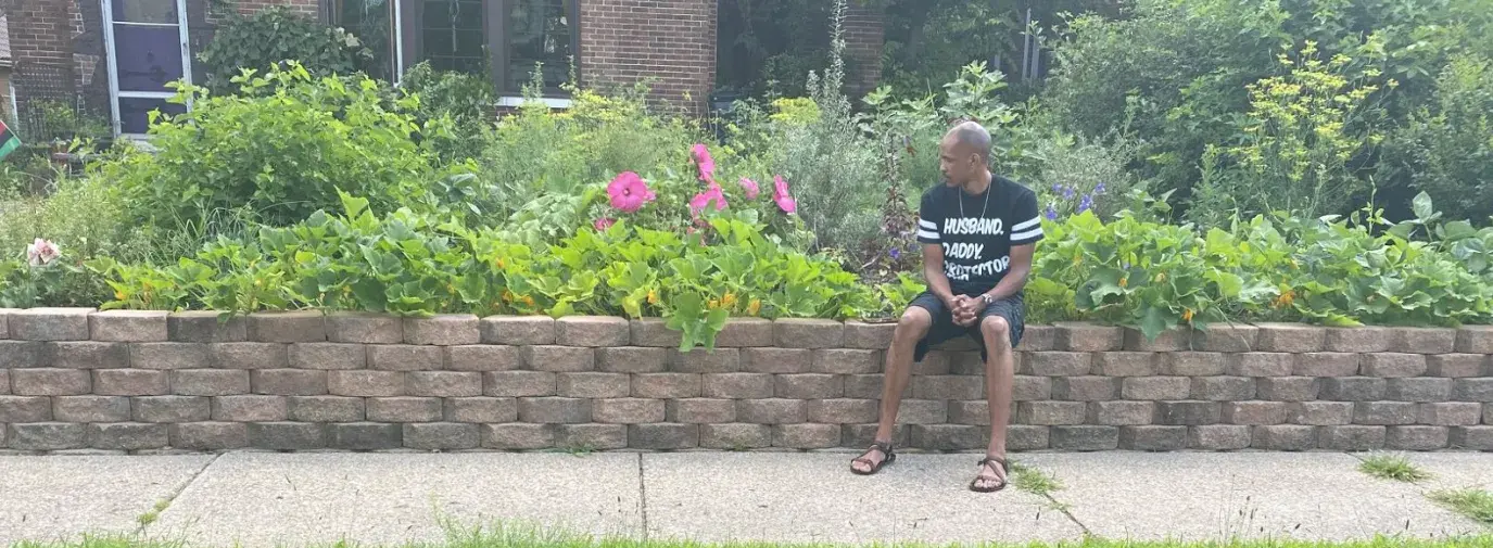 Yasir Allah, Aja Yasir's husband, sits in front of their house and climate victory garden in Gary, Indiana. Photo by Aja Yasir.