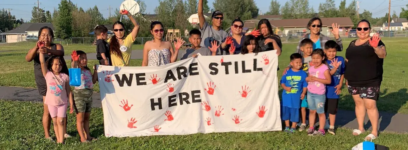 Indigenous activists holding a sign that reads "we are still here"