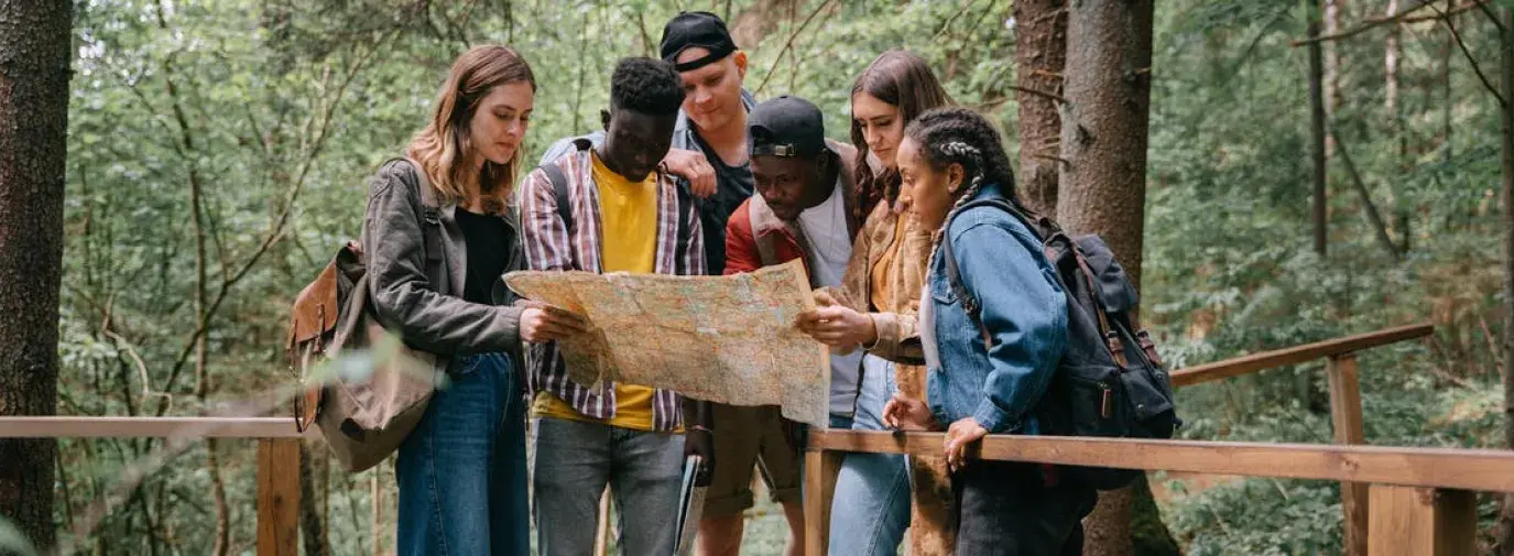 a group of young people on a walking bridge in the woods looking at a map together.