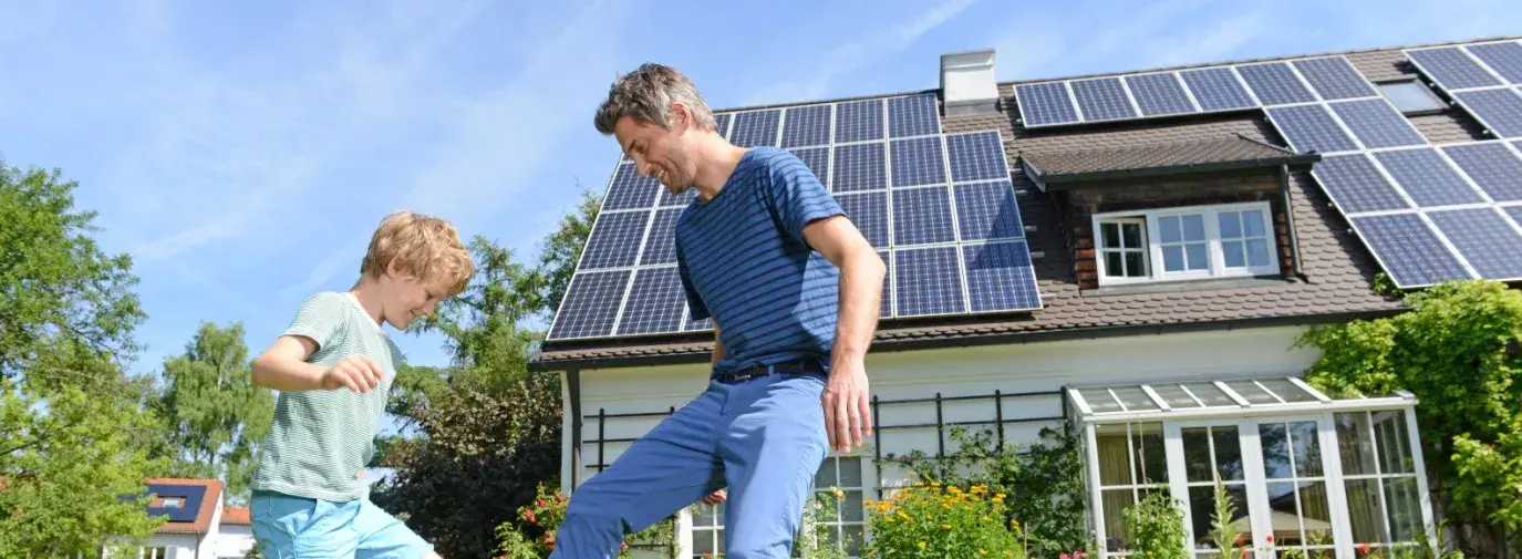 white dad and son playing soccer in the front yard of their house that is covered in solar panels