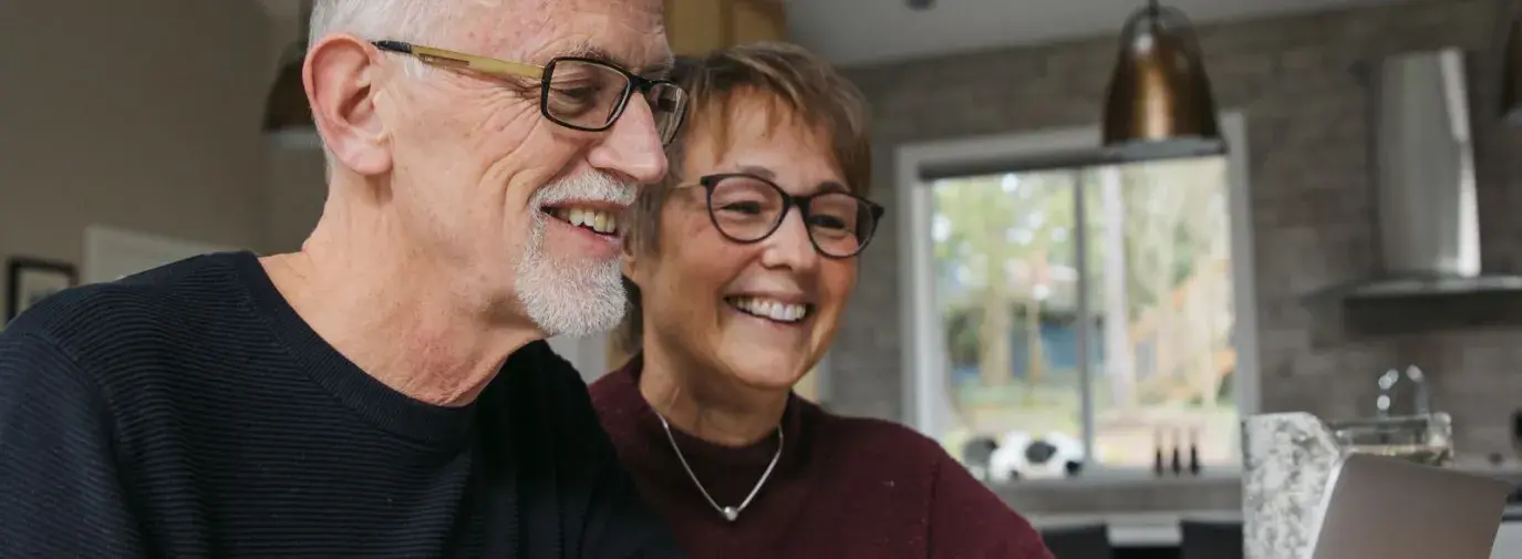 elderly couple looking at a computer screen, smiling. 