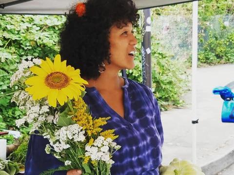 Roberta Eaglehorse-Ortiz stands in the Wombyn's Wellness Garden with a fresh-picked bouquet of goldenrod, sunflowers, and little white flowers.