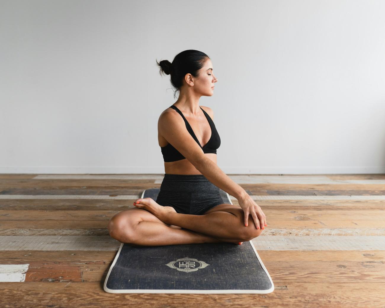 Woman doing yoga on a mat. She sits cross-legged and twists. Sustainable summer.