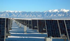 Image: solar panels in a field with snow-capped mountains beyond. Title: Try A Solar Water Heater