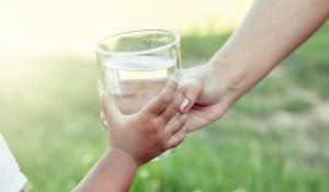 Image: adult handing glass of water to a child. Title: Bottled Water vs. Tap: Which is Best?