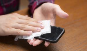 A person wiping down a smartphone with a flushable wipe. 