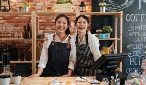 mother and daughter wearing aprons and smiling. They are coffee shop owners ready to make coffee.