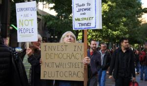 A people's march with signs that read "Invest in democracy, not wall street plutocracy" and "corporations are not people".