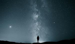 the silhouette of a person in the dark, looking up at the milky way.