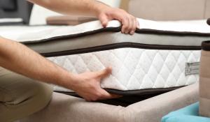 two hands lifting and placing a mattress on a bedframe