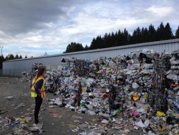 Image: person standing in front of large piles of recyclables. Topic: Does Recycling Help the Climate?