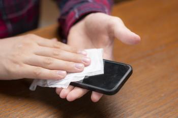 A person wiping down a smartphone with a flushable wipe. 