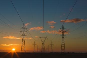 Sunset behind power lines and towers, which do not prioritize energy efficiency