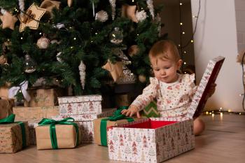 A baby opening Christmas presents in front of a decorated tree. The presents are in boxes and brown paper. Fair Trade Gift Guide.