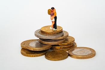 Two clay figures in a romantic embrace stand atop a pile of gold coins. Valentine's Day love money.