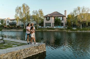 Two women stand with their arms around a young girl, their daughter, at the edge of a small lake with homes and trees in the background. Clean energy for all.