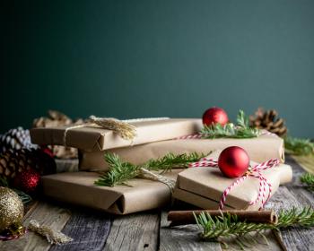 Gifts wrapped in brown paper with pine and ornaments around them. Sustainable gifts holidays.